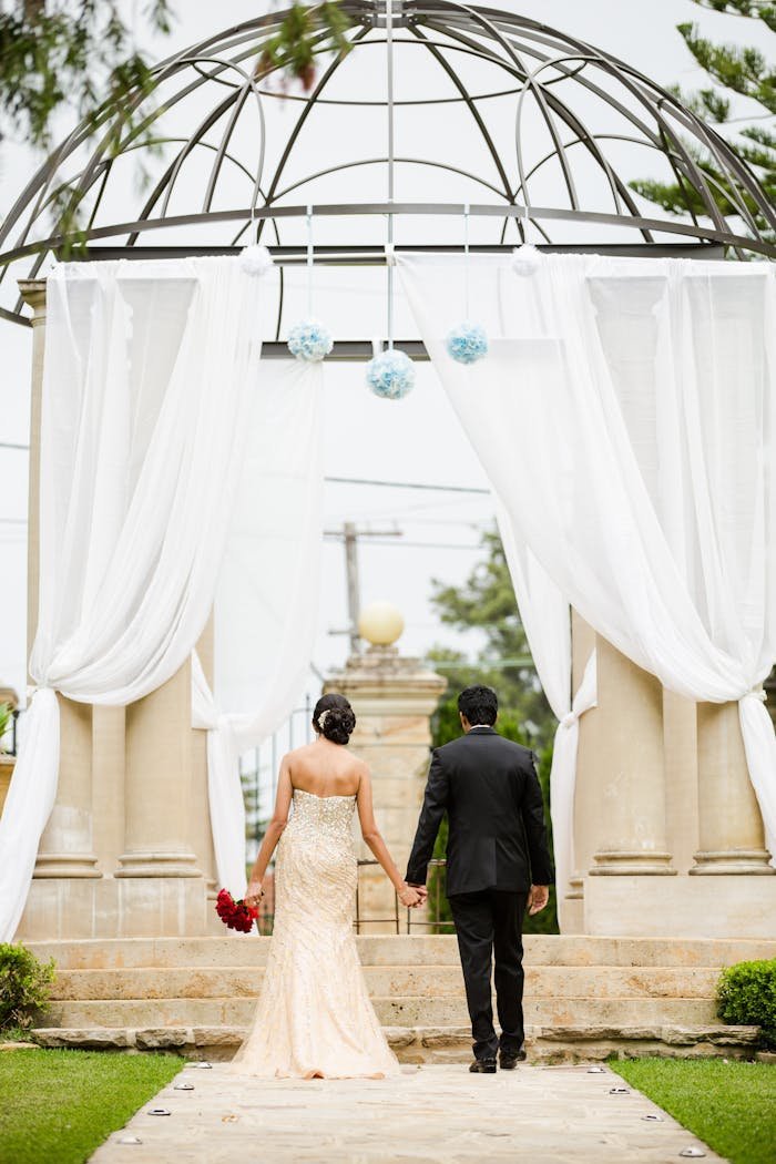 A couple holding hands, walking towards an elegant outdoor wedding arch in Marsfield, NSW.